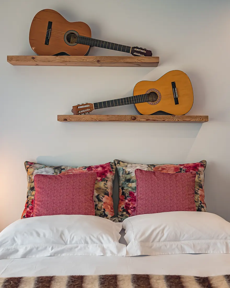 Bedroom of a property managed by Alojoeste, with guitars on the wall and white bed linen.