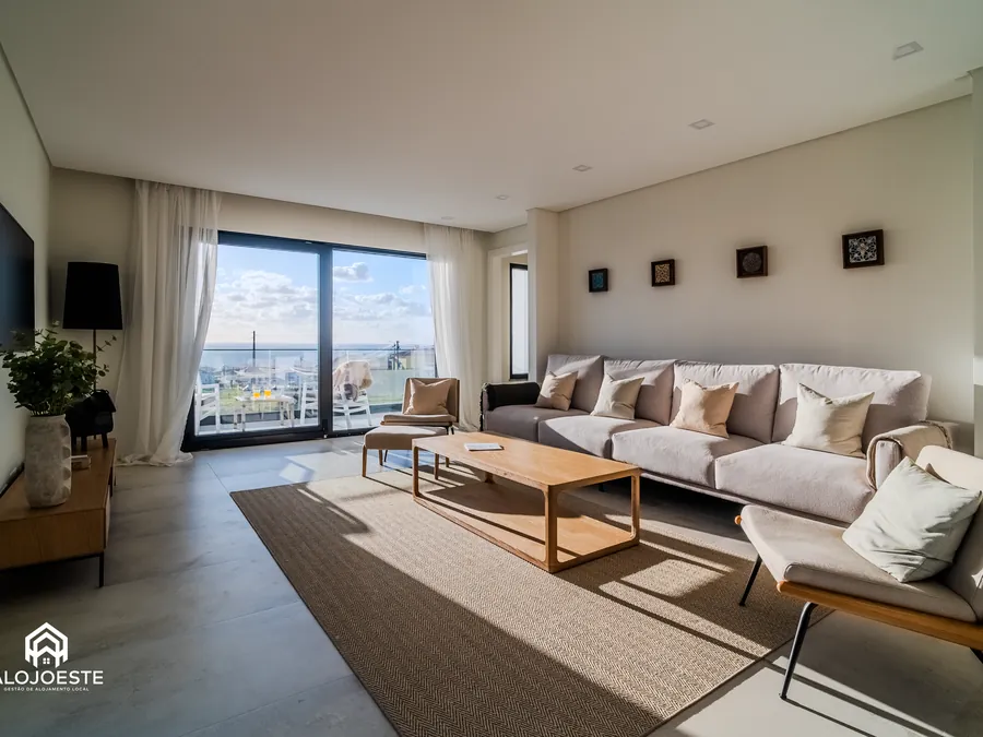 Living room of a property managed by Alojoeste, with pale sofas and a sea view.